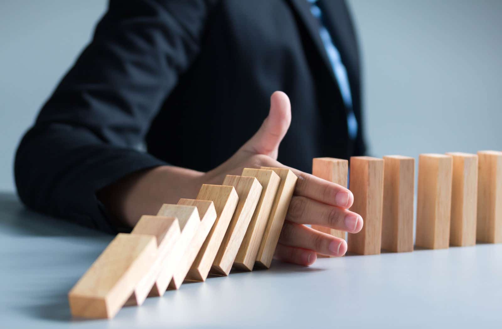 Falling dominoes blocked from cascading further by a businessman's hand.