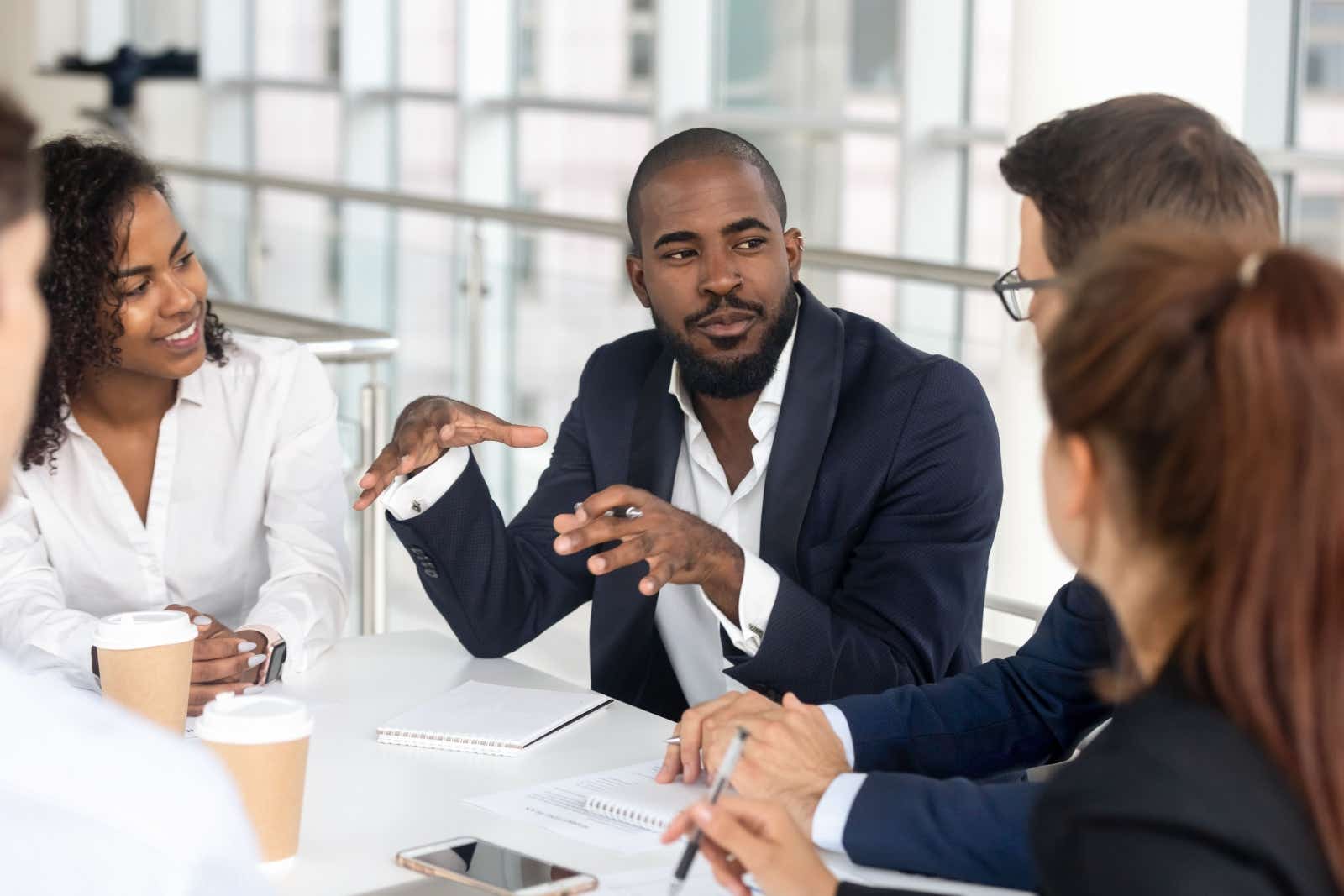 Business team gathered around a table listening to one person