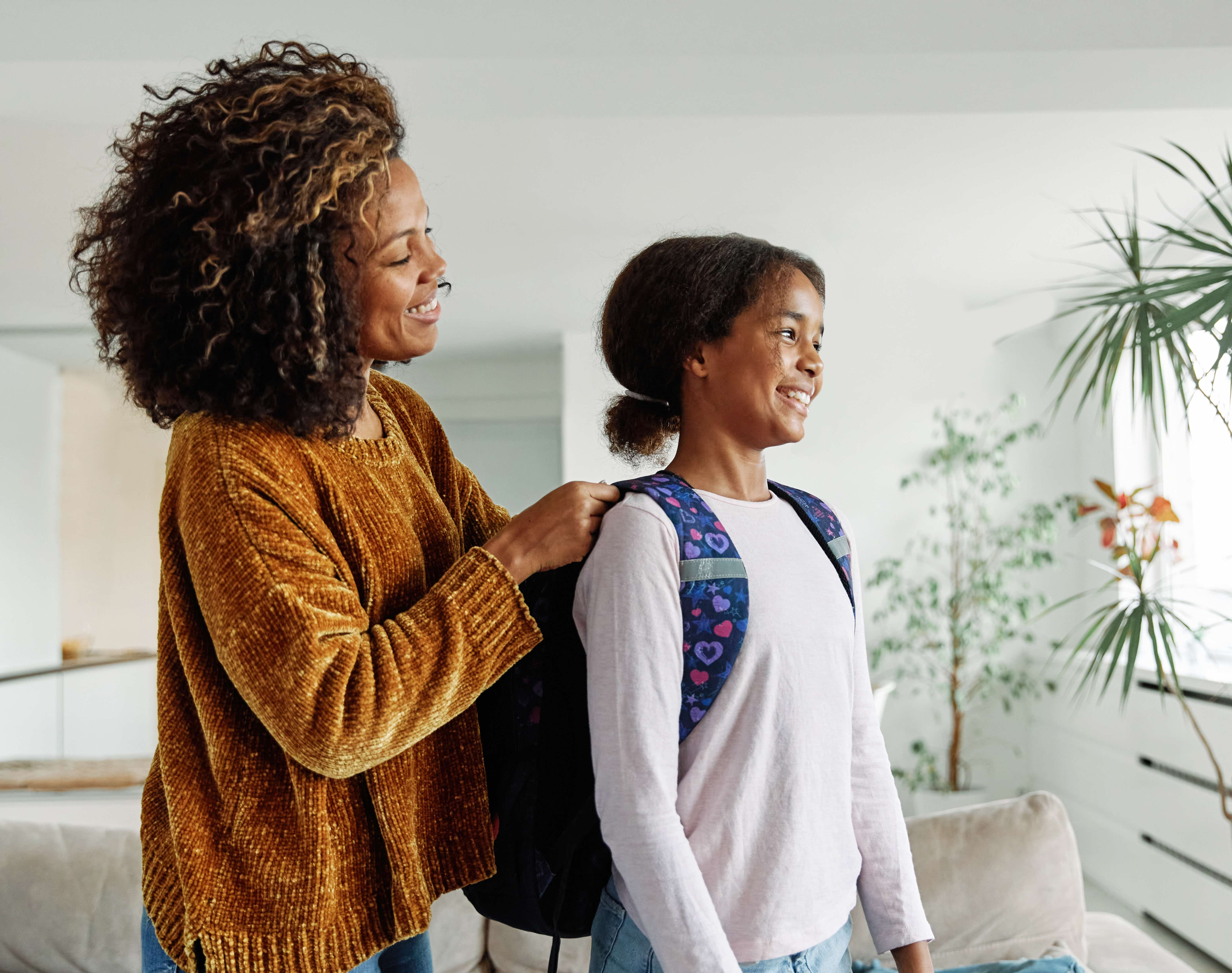Mother helping daughter to get ready for school, helping her with backpack and books.