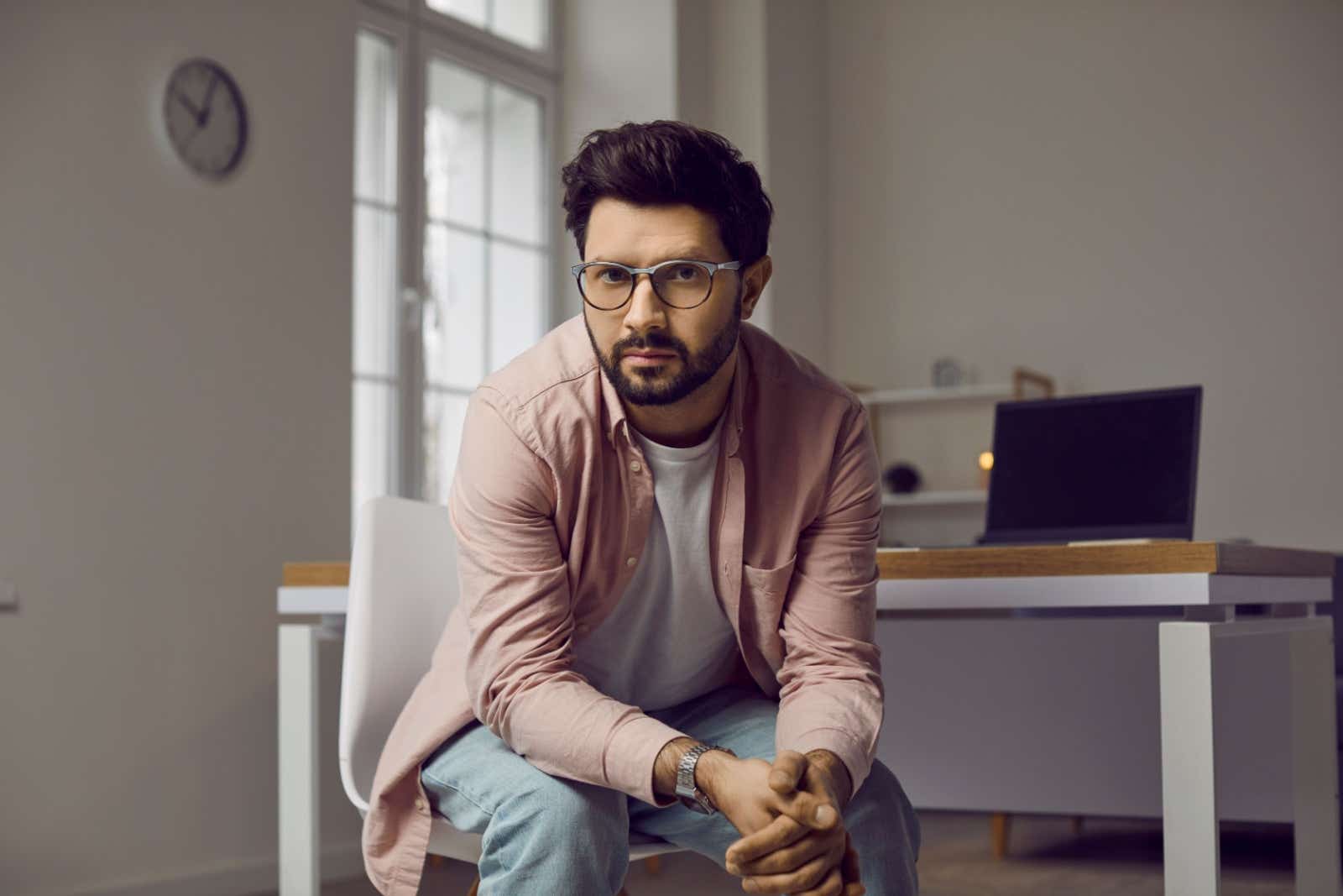 Man sits looking at the camera with a laptop and home office in the background.