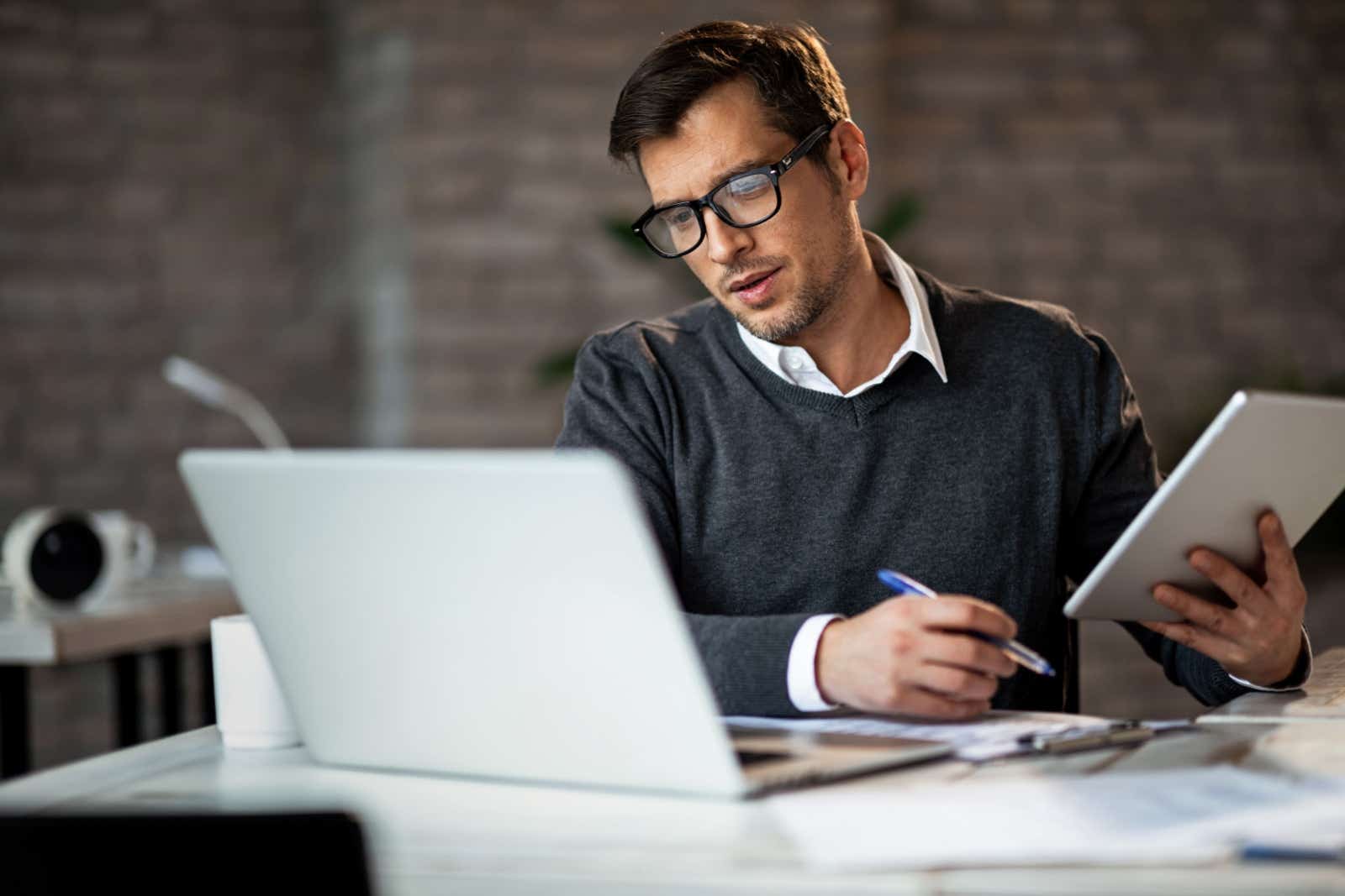 Casually dressed businessman looking at laptop while holding a pad and pen.