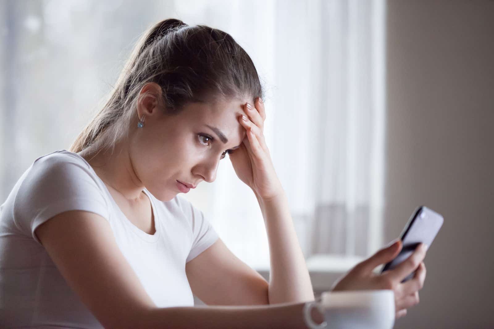 Young woman looking depressed as she looks at her phone.