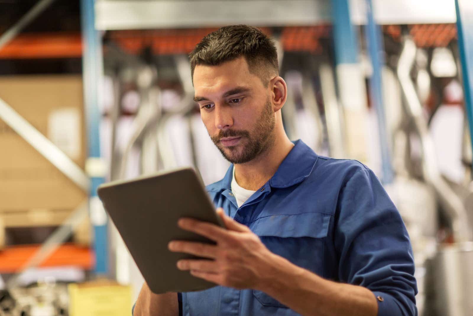 Man in overalls in a garage looking at his tablet.